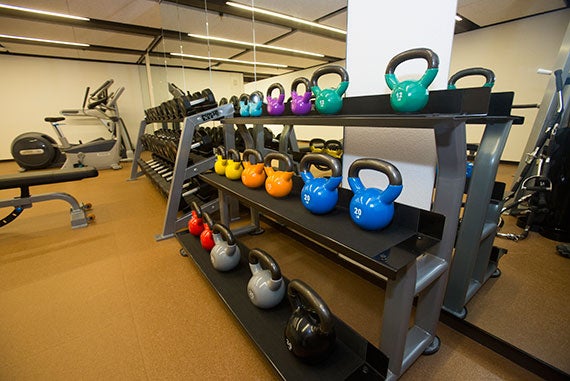 Colorful kettlebells, weights, and cardio machines fill the exercise room.