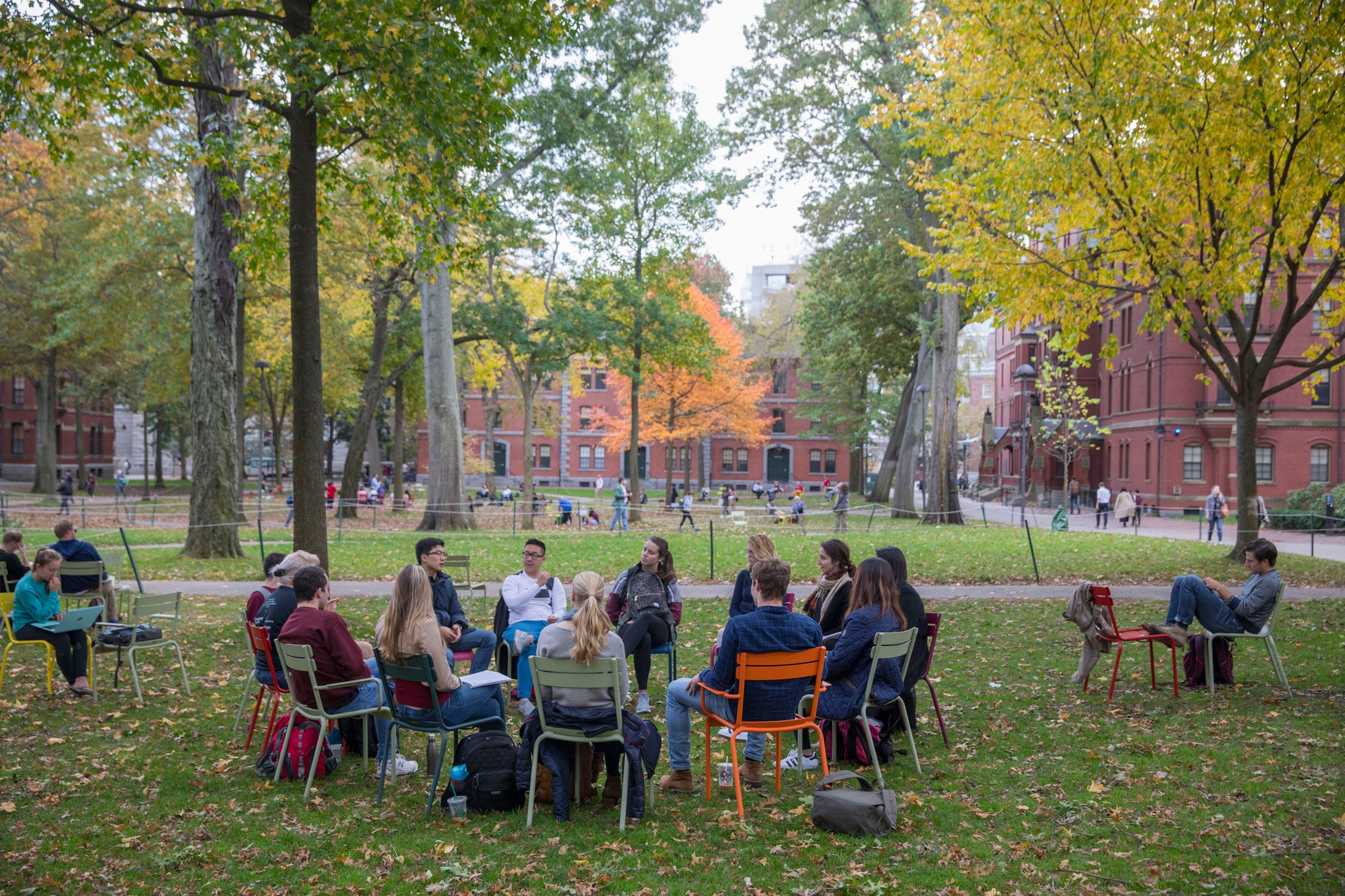 A circle of students sit in chairs in Harvard Yard.
