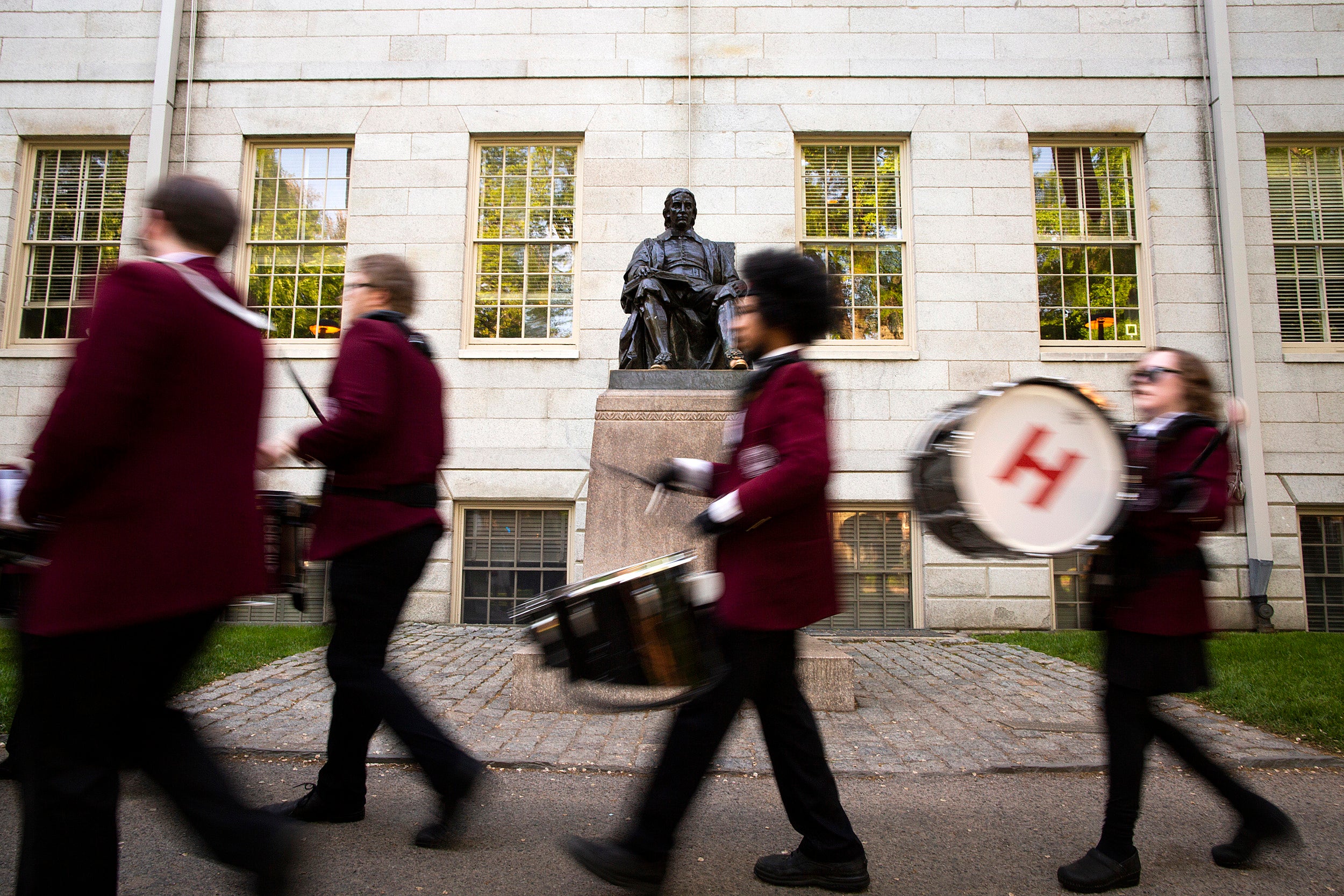 Graduates walk past John Harvard Statue.
