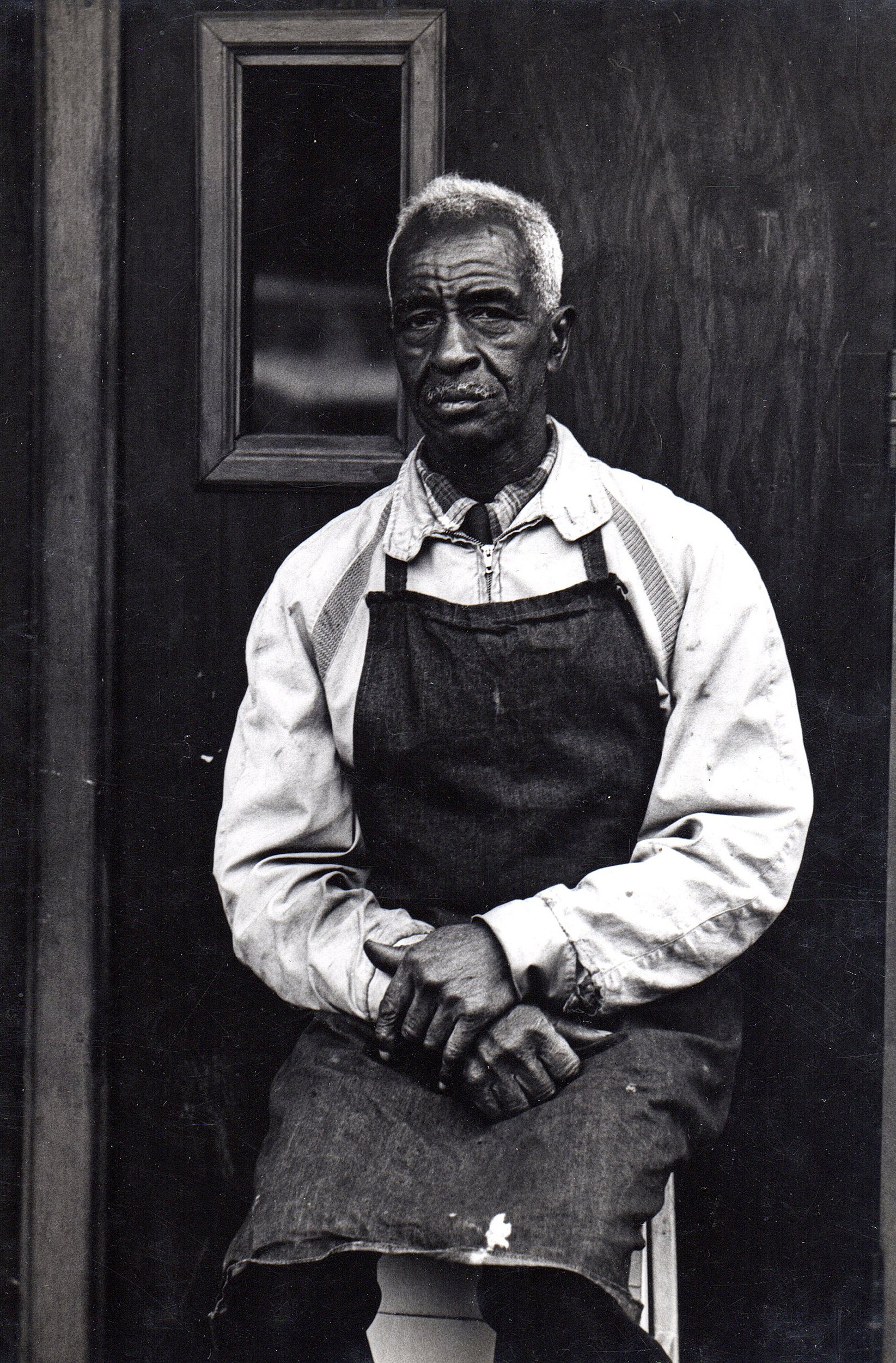 Man wearing apron seated on Blake Avenue in New York, 1965.