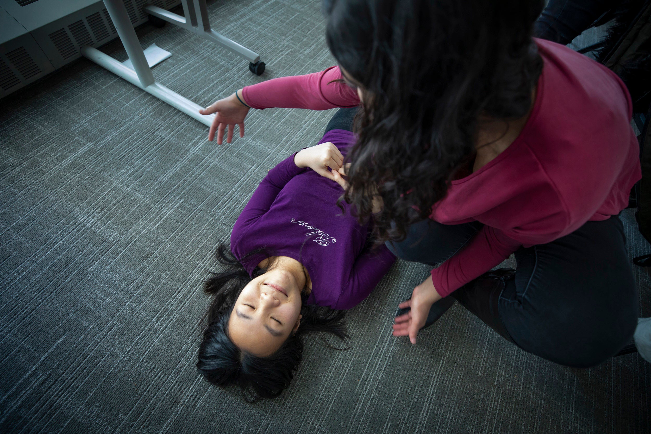 A student lies on the floor as another checks for bleeding.