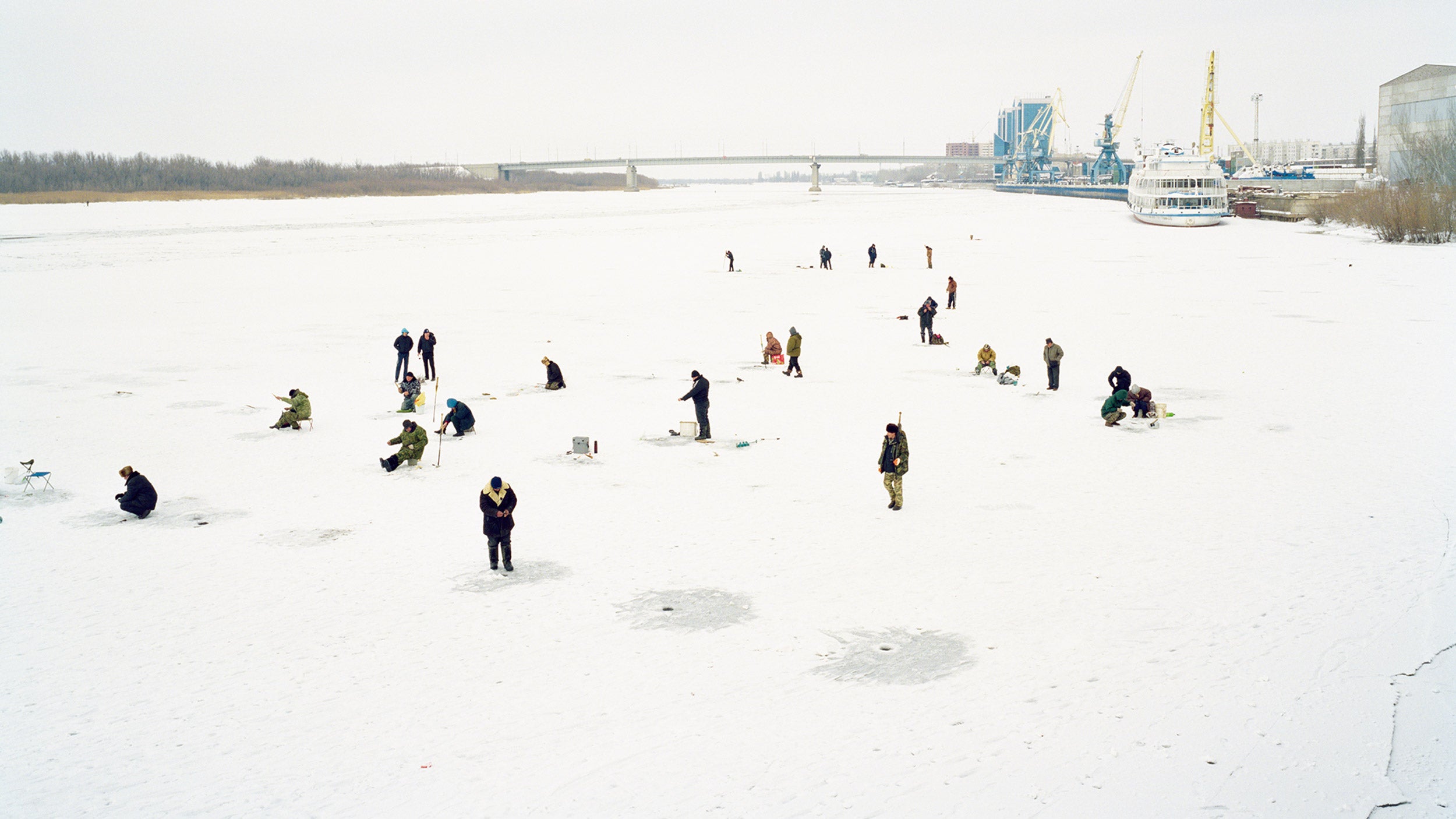 Fishermen cut holes in frozen river on the outskirts of the city, Astrakhan, Russia.