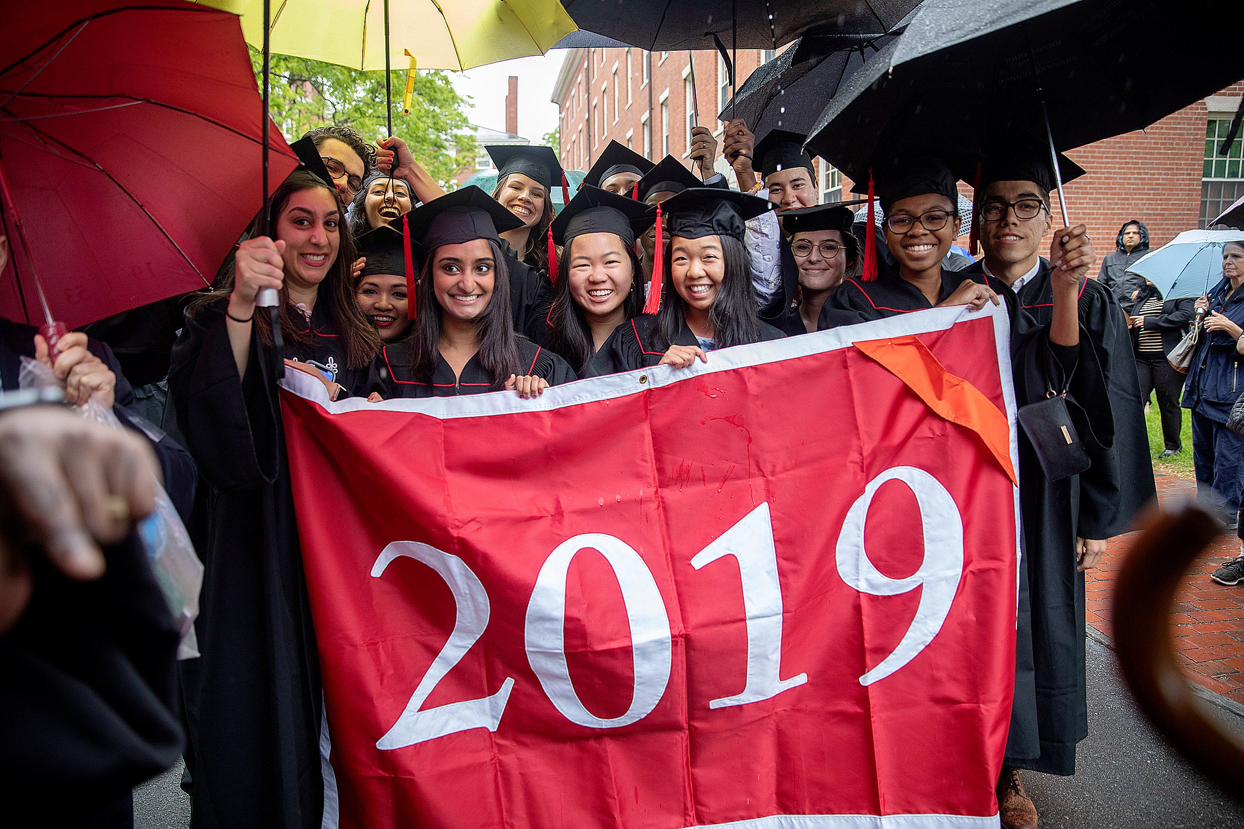 The Baccalaureate procession marches toward Memorial Church holding a 2019 banner and umbrellas.
