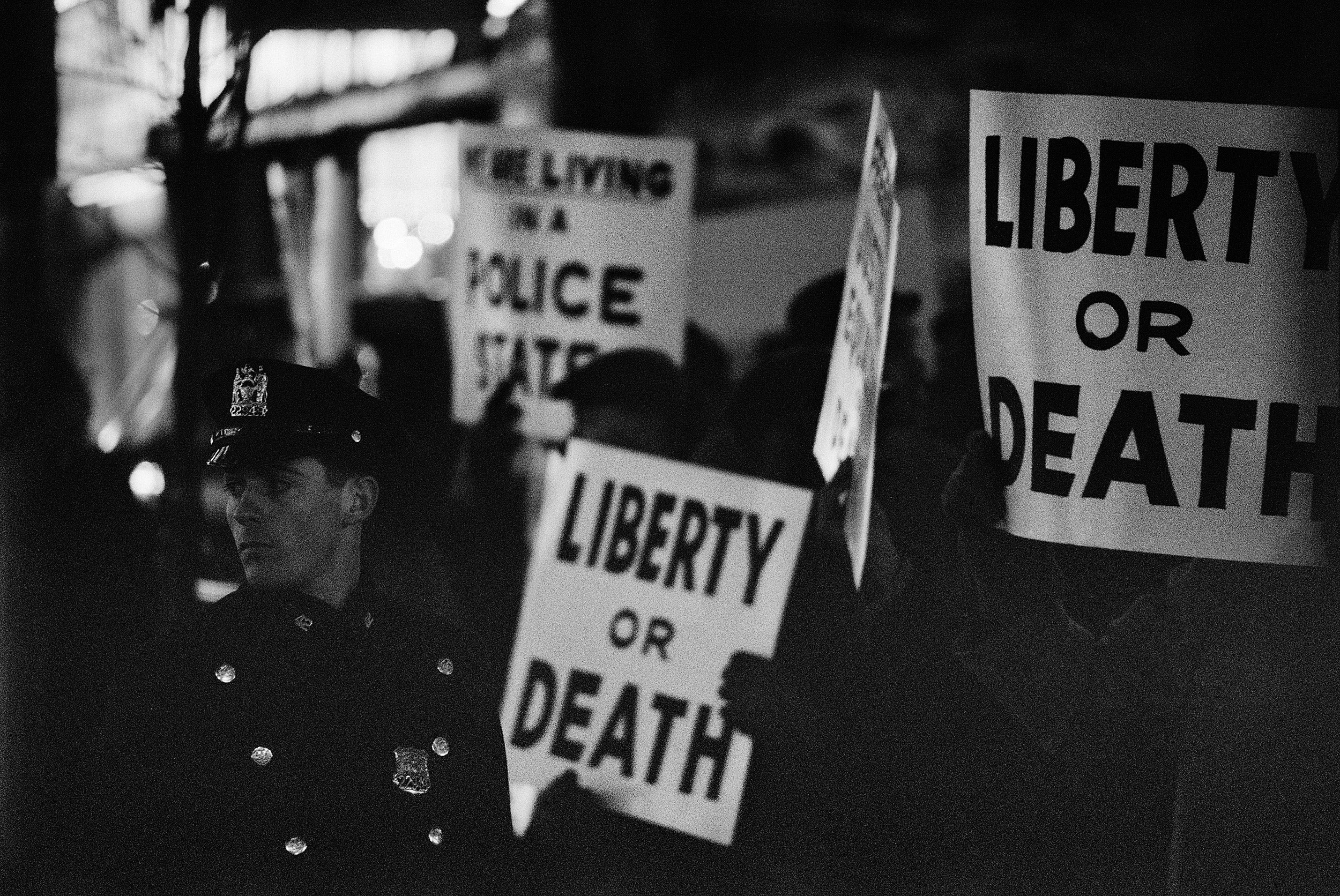 "Liberty or death" on posters in the background, a police officer in the foreground