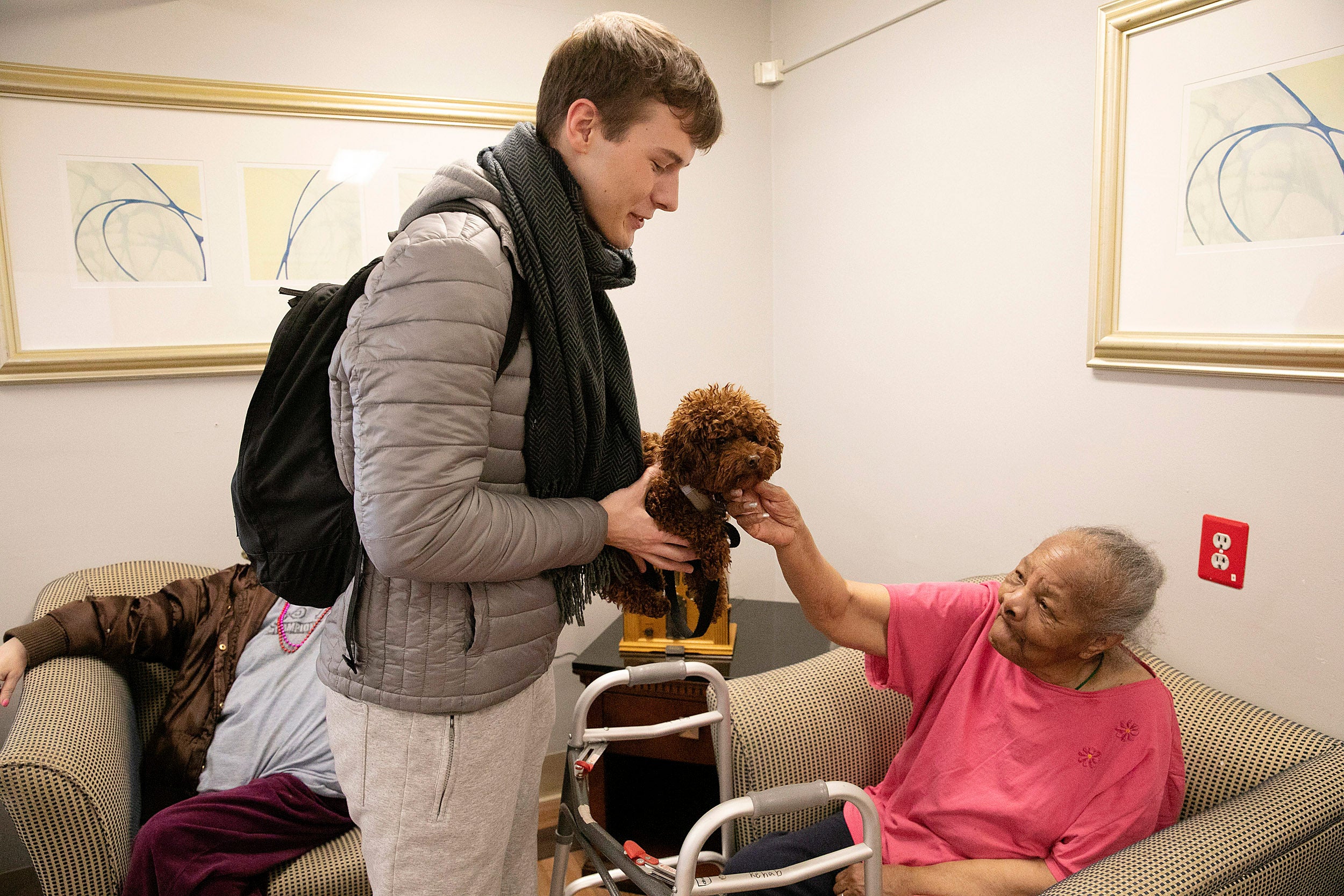 Student holds dog while elderly woman pat dog.