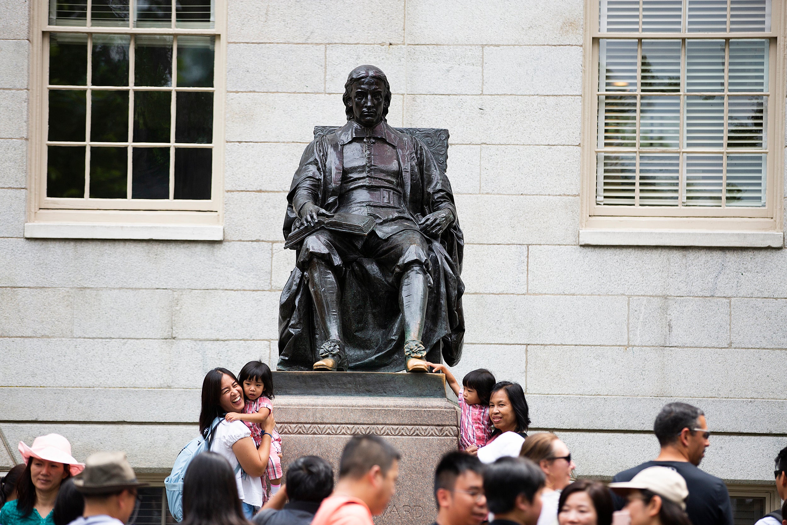 Visitors crowd the John Harvard statue, raising children to touch the foot.