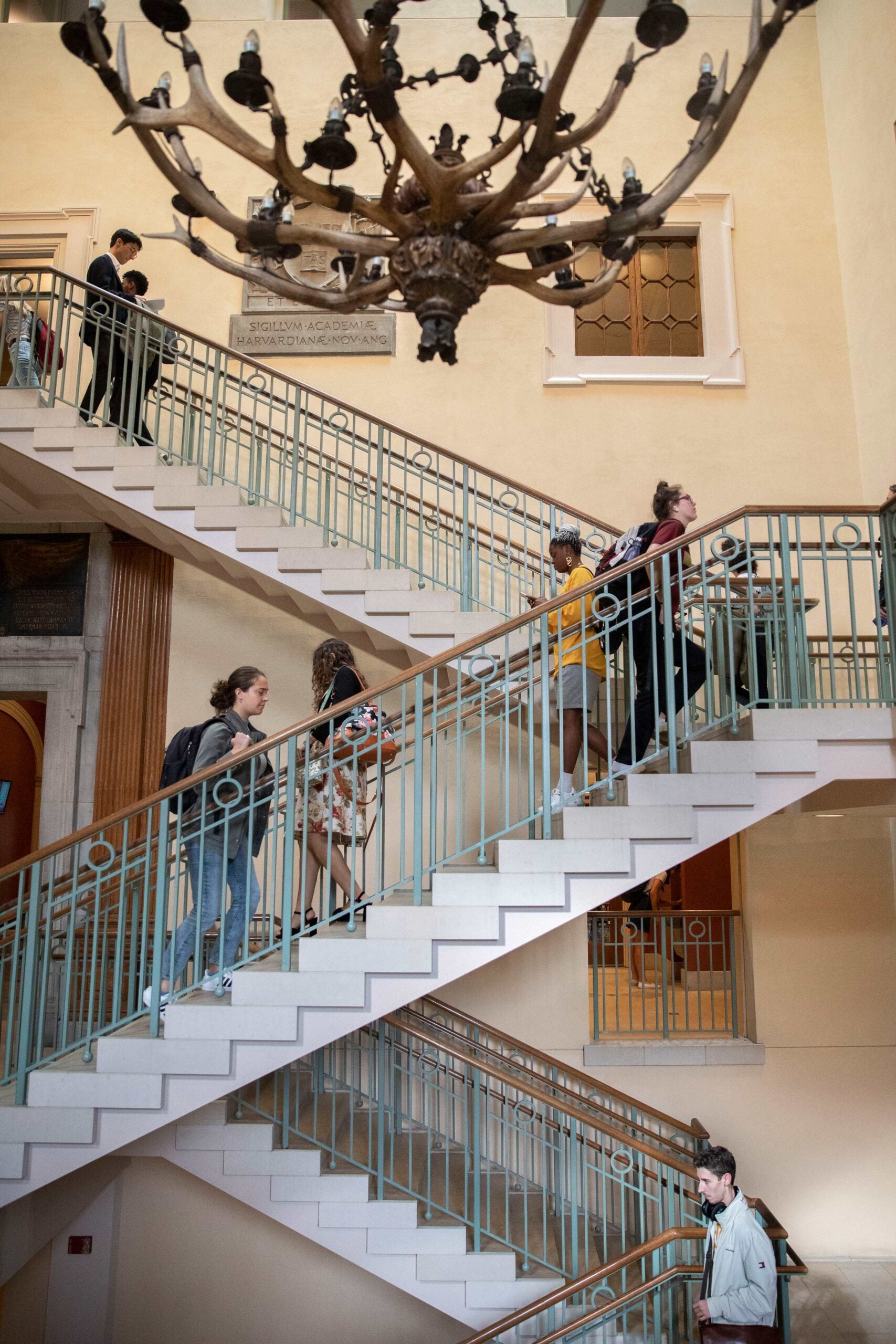 Students walking up and down a three level staircase under a decorative chandelier.