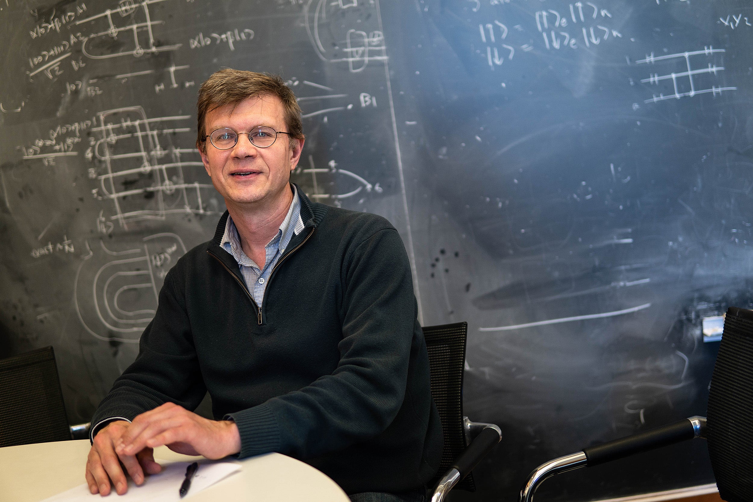 Professor Mikhail Lukin, co-director of Harvard’s Quantum Initiative, in his classroom with a blackboard filed with equations.