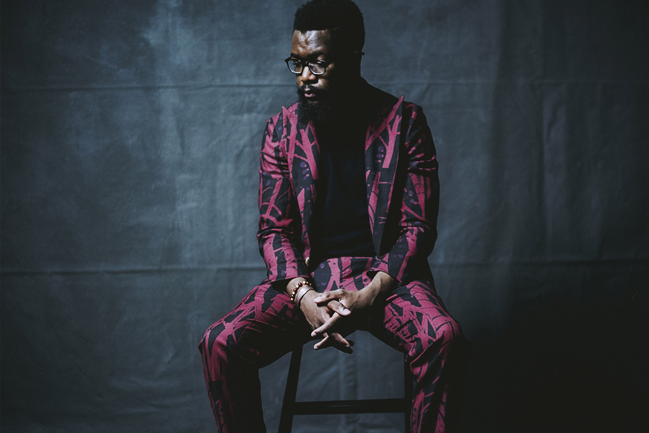 Male model sitting on a stool in a brightly patterned suit.