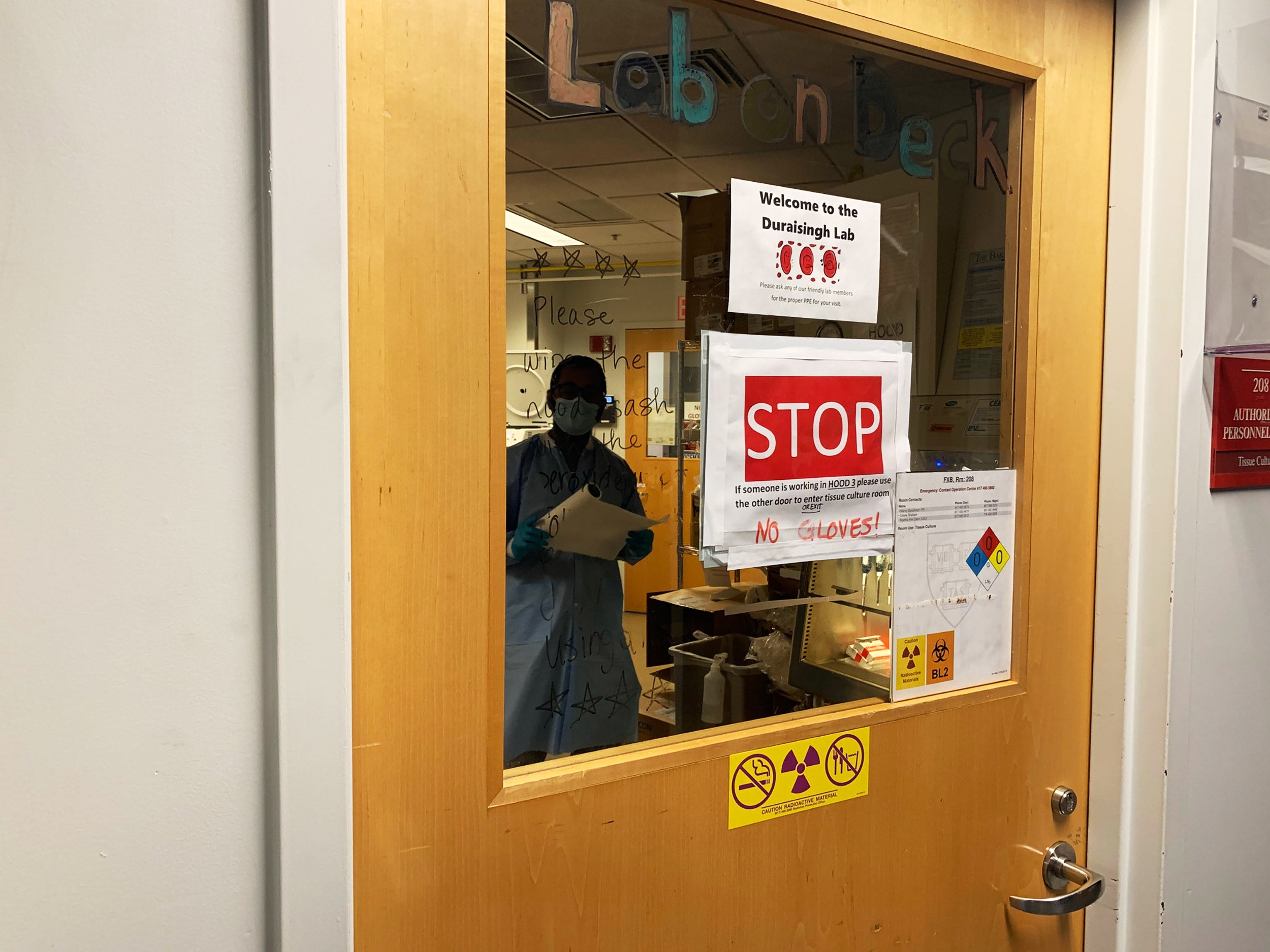 Researcher viewed through lab door posted with safety signs.