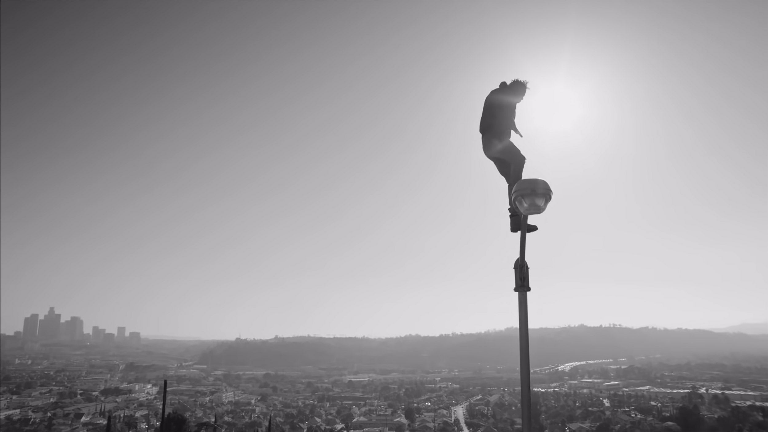 Kendrick Lamar stands on lamppost towering over L.A. skyline in "Alright" video.