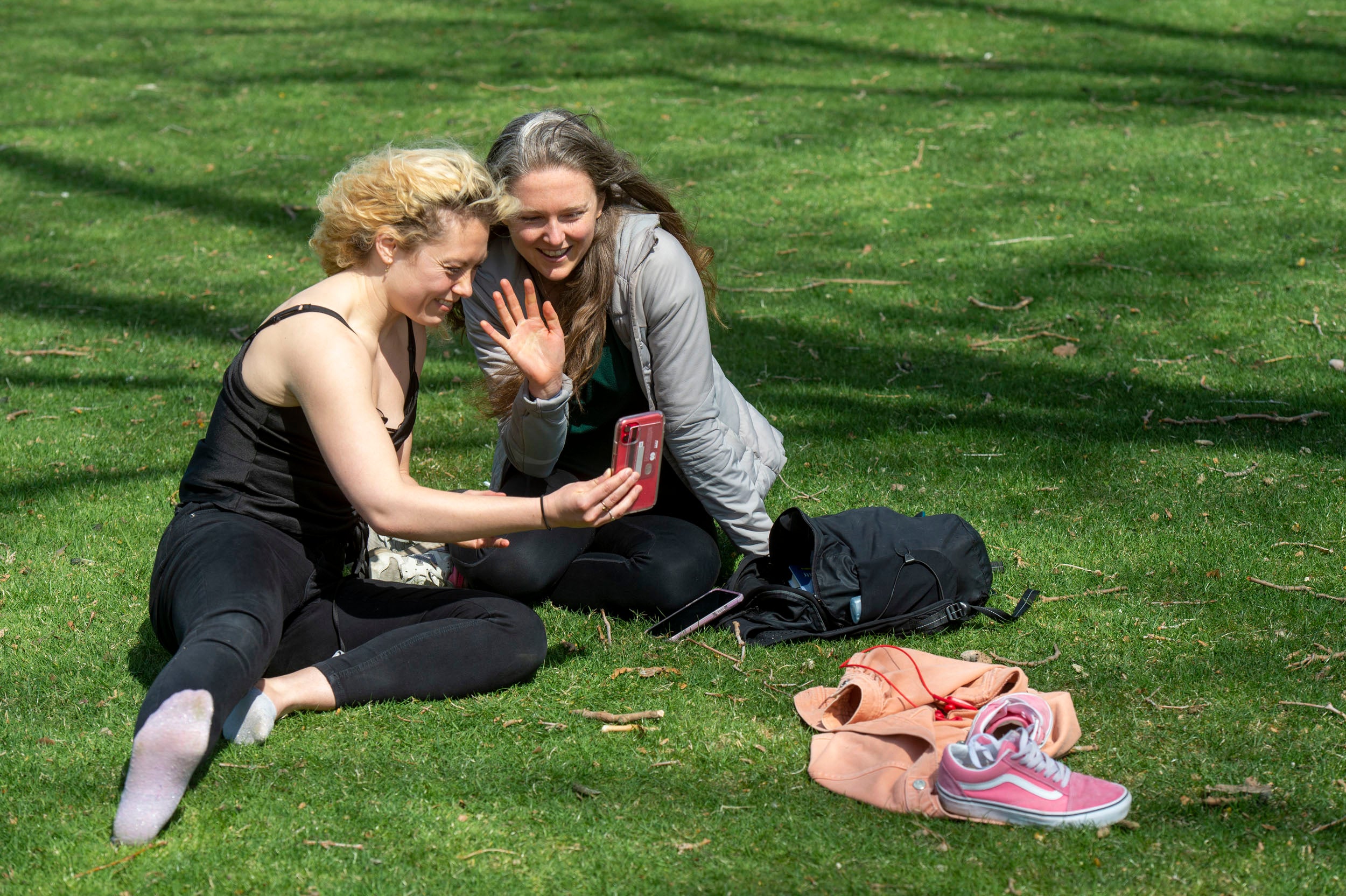 Grace Birch and Whitney McFadden FaceTime with a friend while relaxing on the HKS lawn adjacent to Memorial Drive.