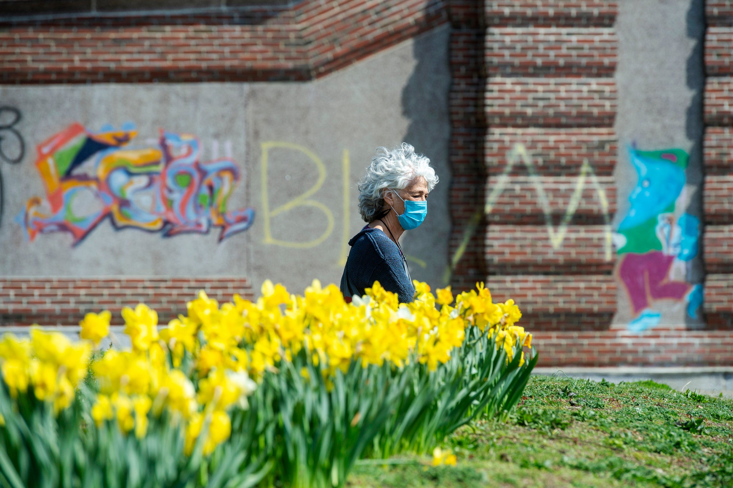 Cambridge resident Amy Rugel soaks up some sun by a row of daffodils at the Anderson Memorial Bridge.