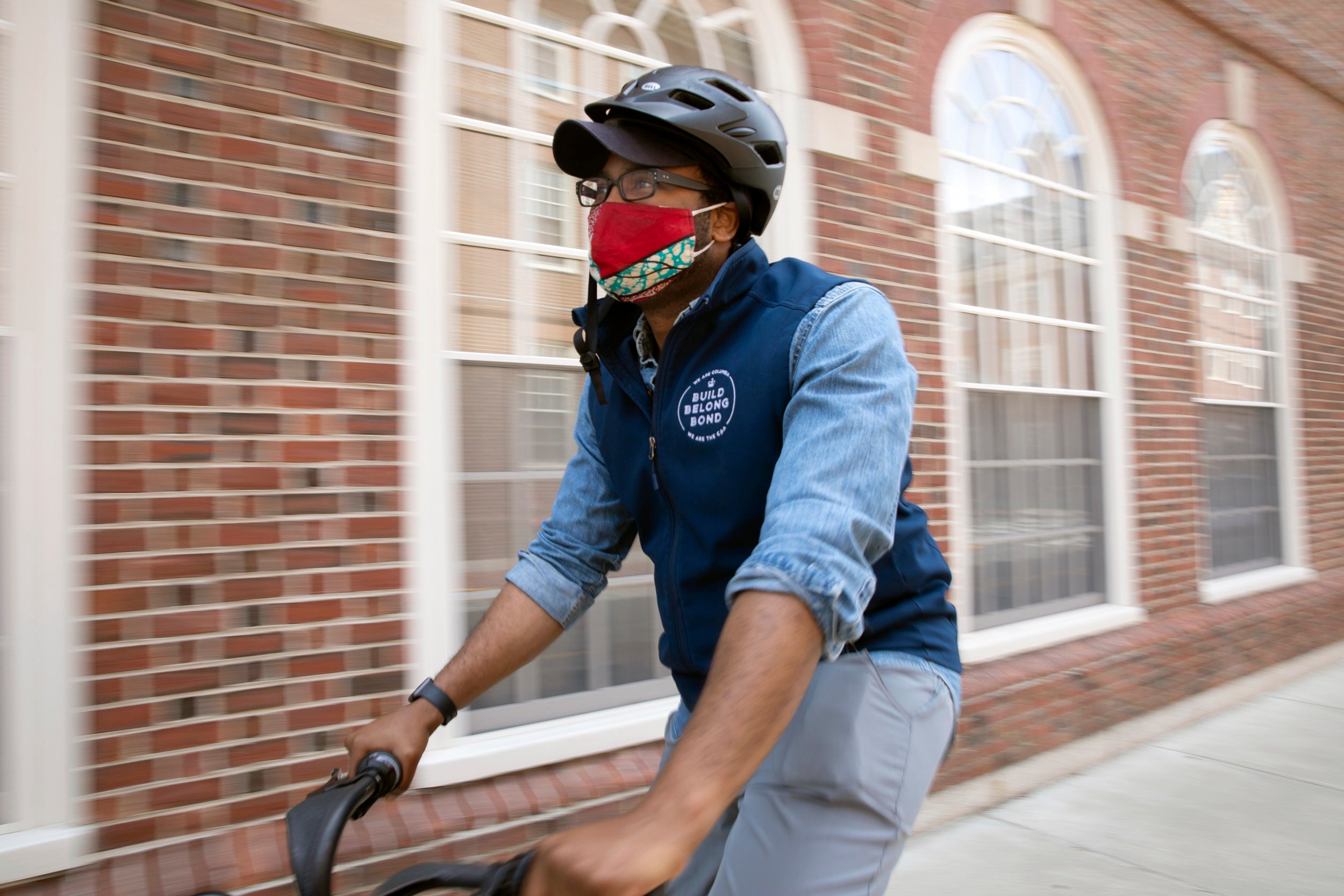 Darold Cuba, Harvard Kennedy School Mid career MPA rides a blue bike near Leverett House.