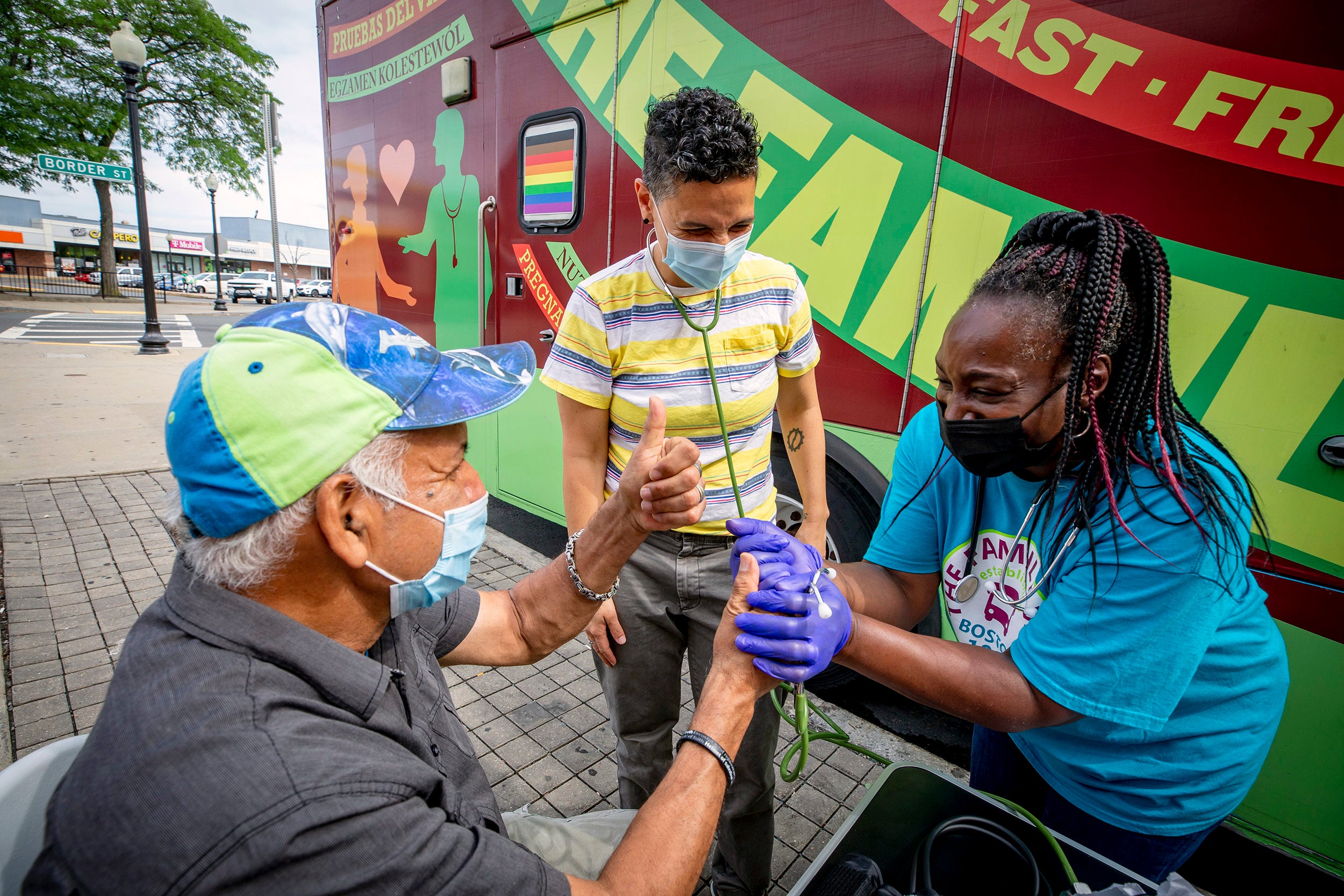Simone de Oliveira, center and Rainelle Walker White, right, assistant director, work together to administer a blood pressure test to Wilson Viana Silva of E. Boston at Harvard University's Family Van.
