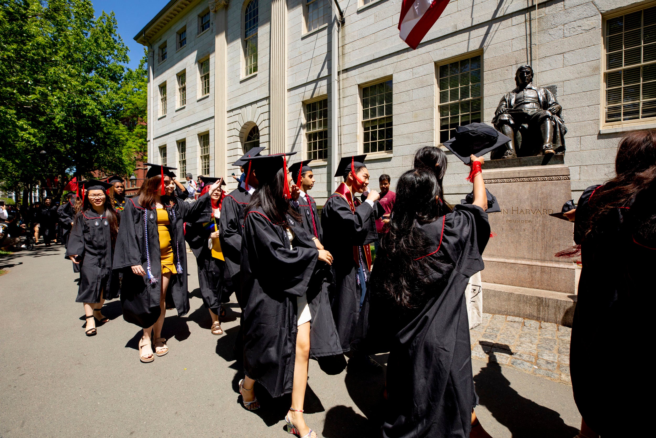 Seniors walking past the John Harvard Statue.