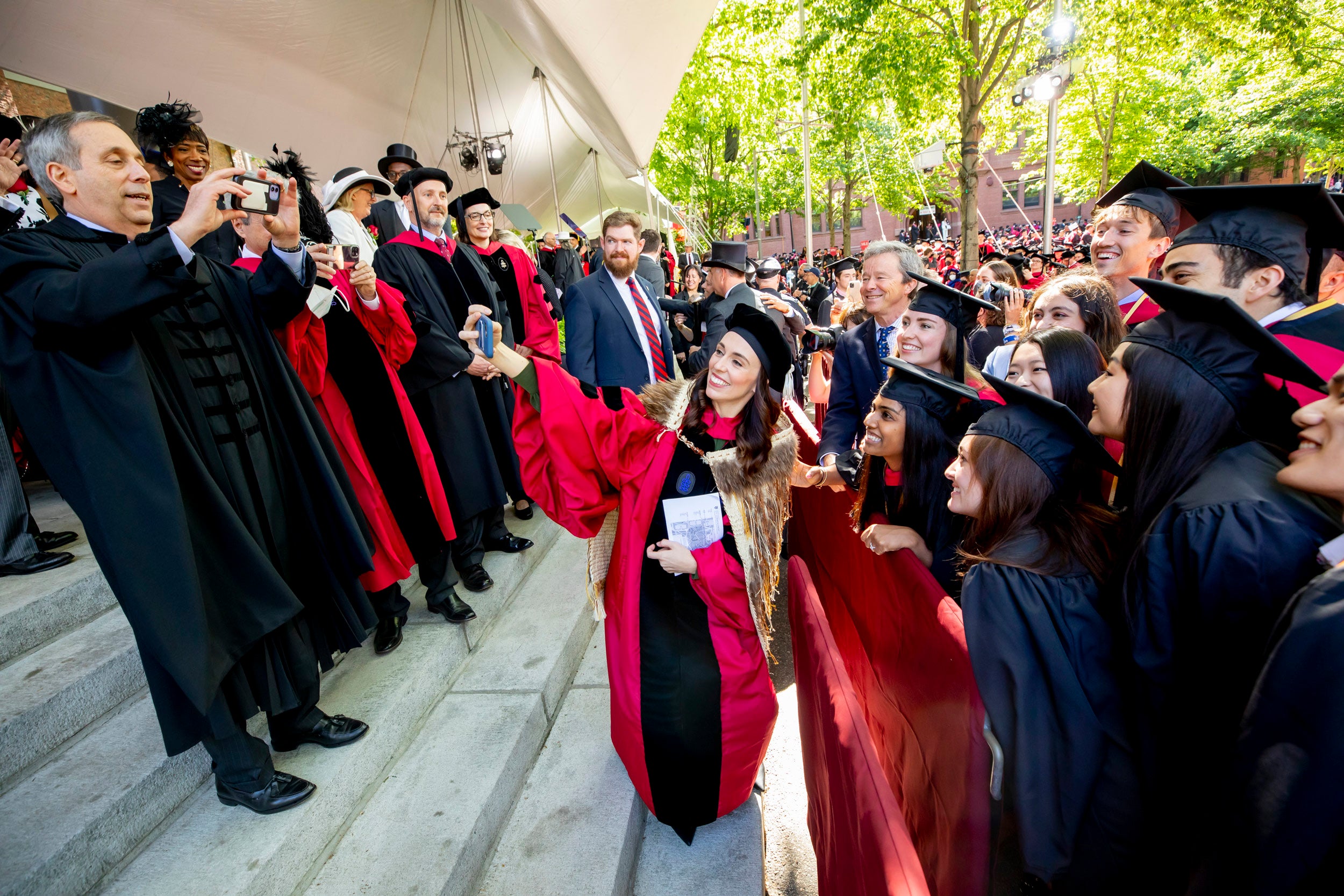 Harvard University President Larry Bacow and New Zealand Prime Minister Jacinda Ardern take photos with graduates before the ceremony begins.