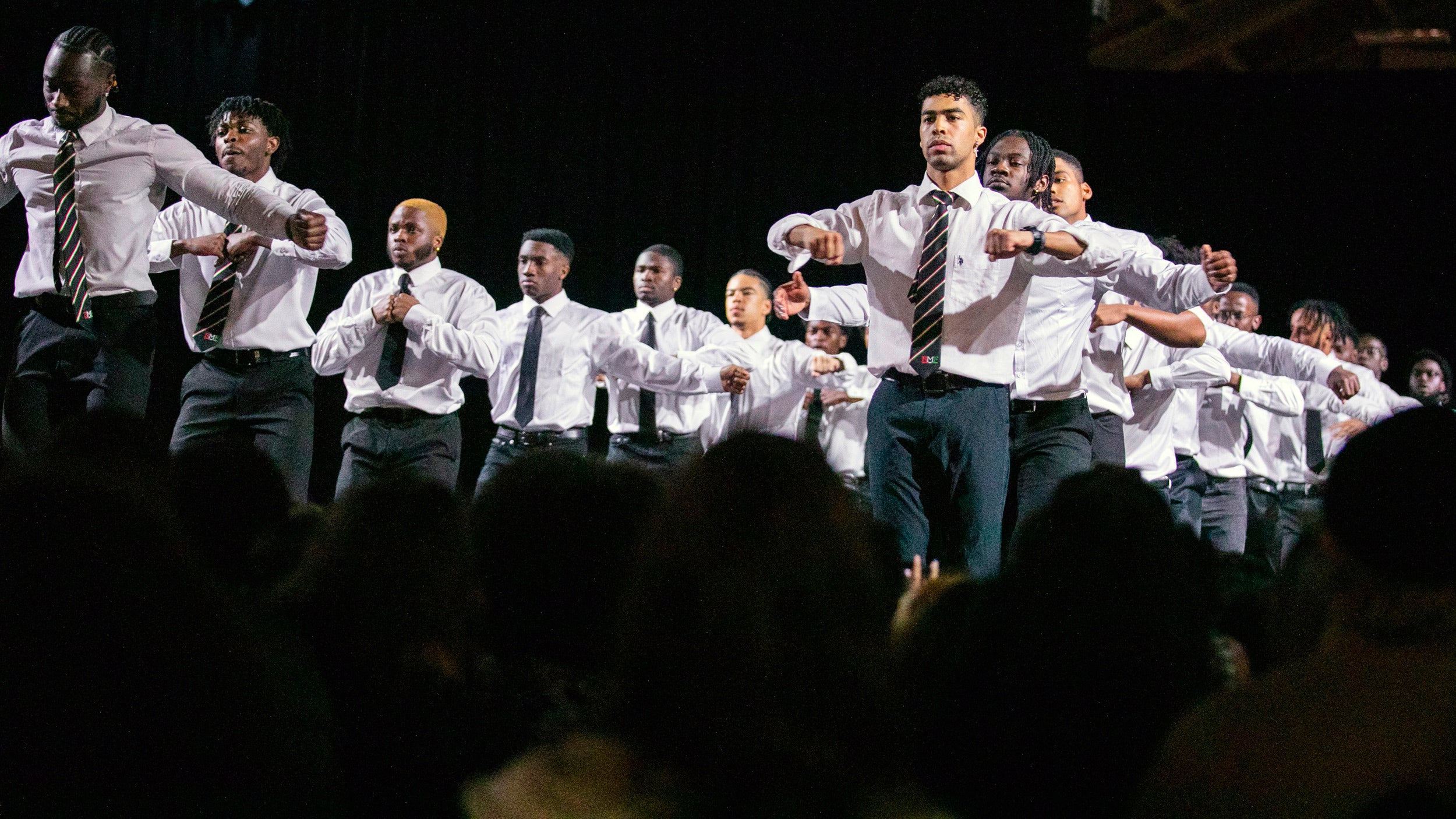 Men in white shirts and ties perform.