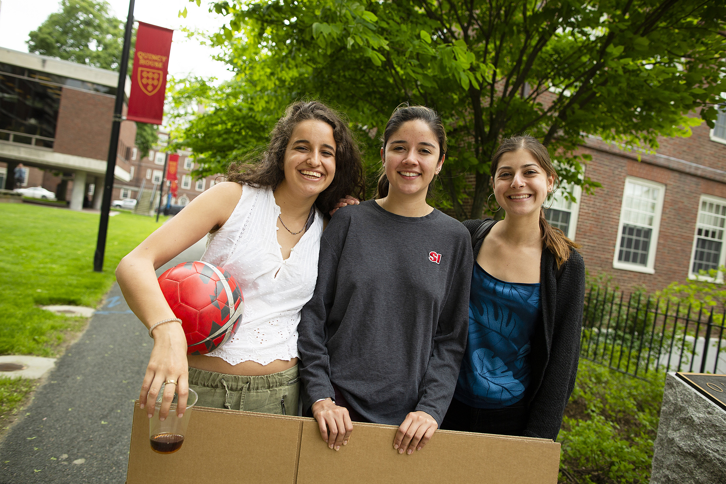 Three friends hold a cardboard poster in the Quincy House courtyard
