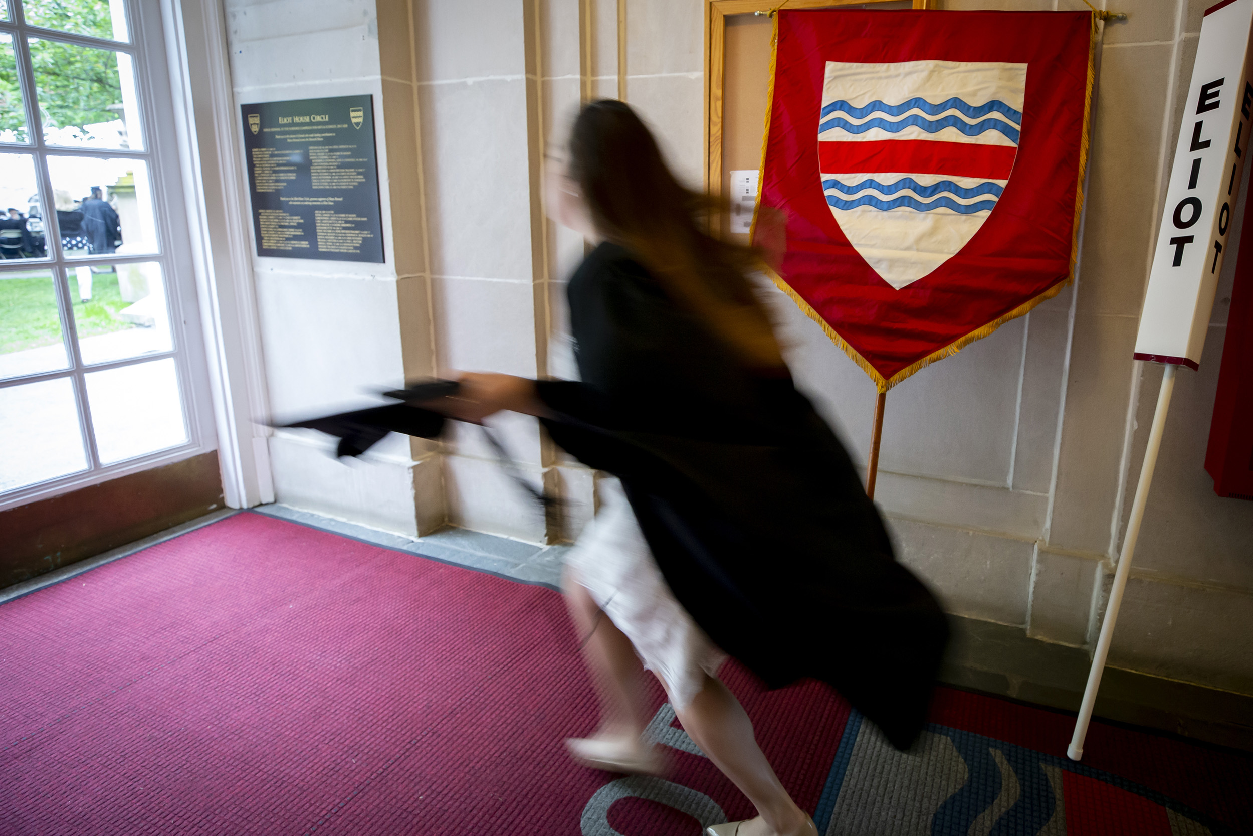 A students runs past an Elliot House shield on Commencement Day.