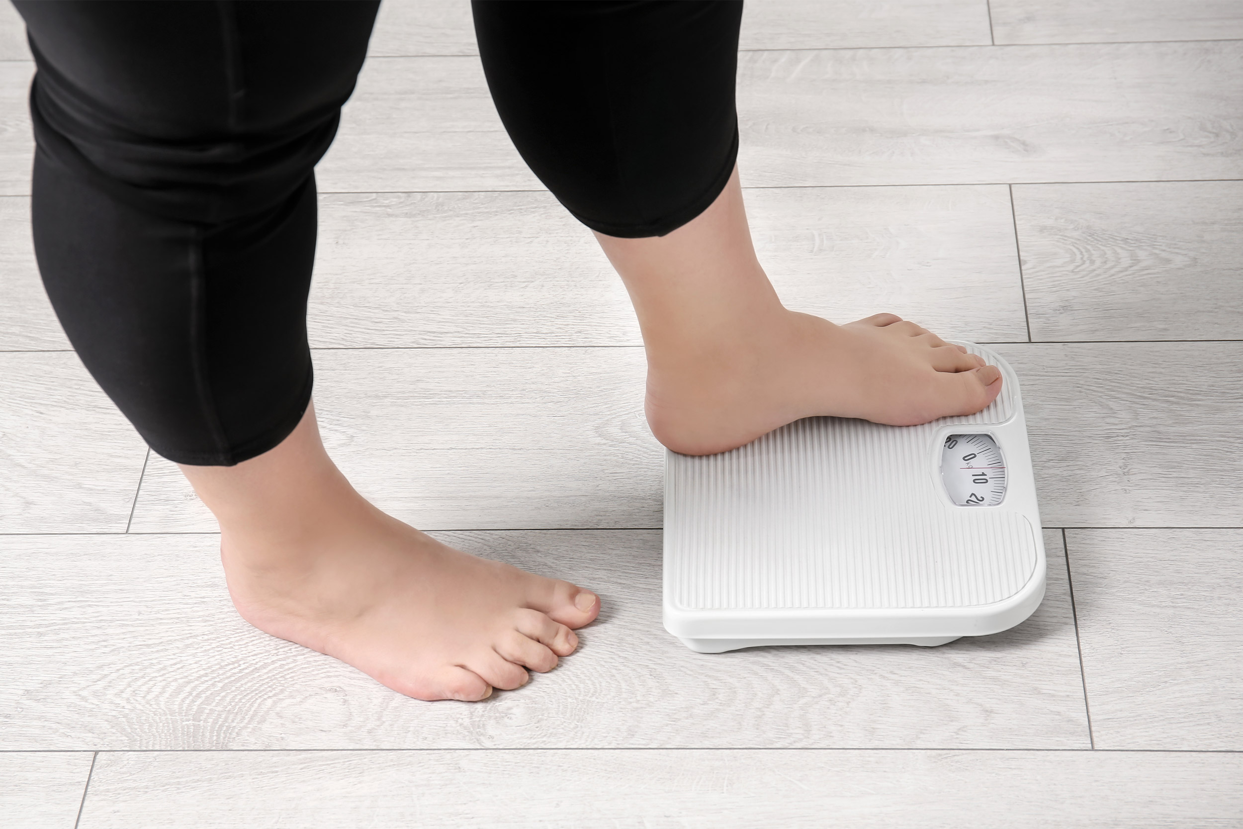 Overweight woman using scales indoors.