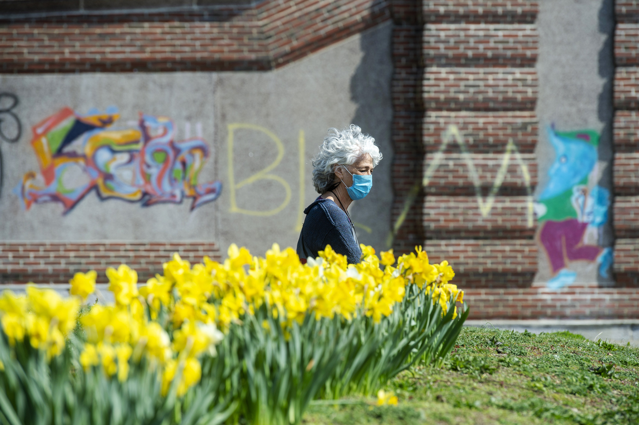 Cambridge resident Amy Rugel soaks up some sun by a row of daffodils at the Anderson Memorial Bridge.