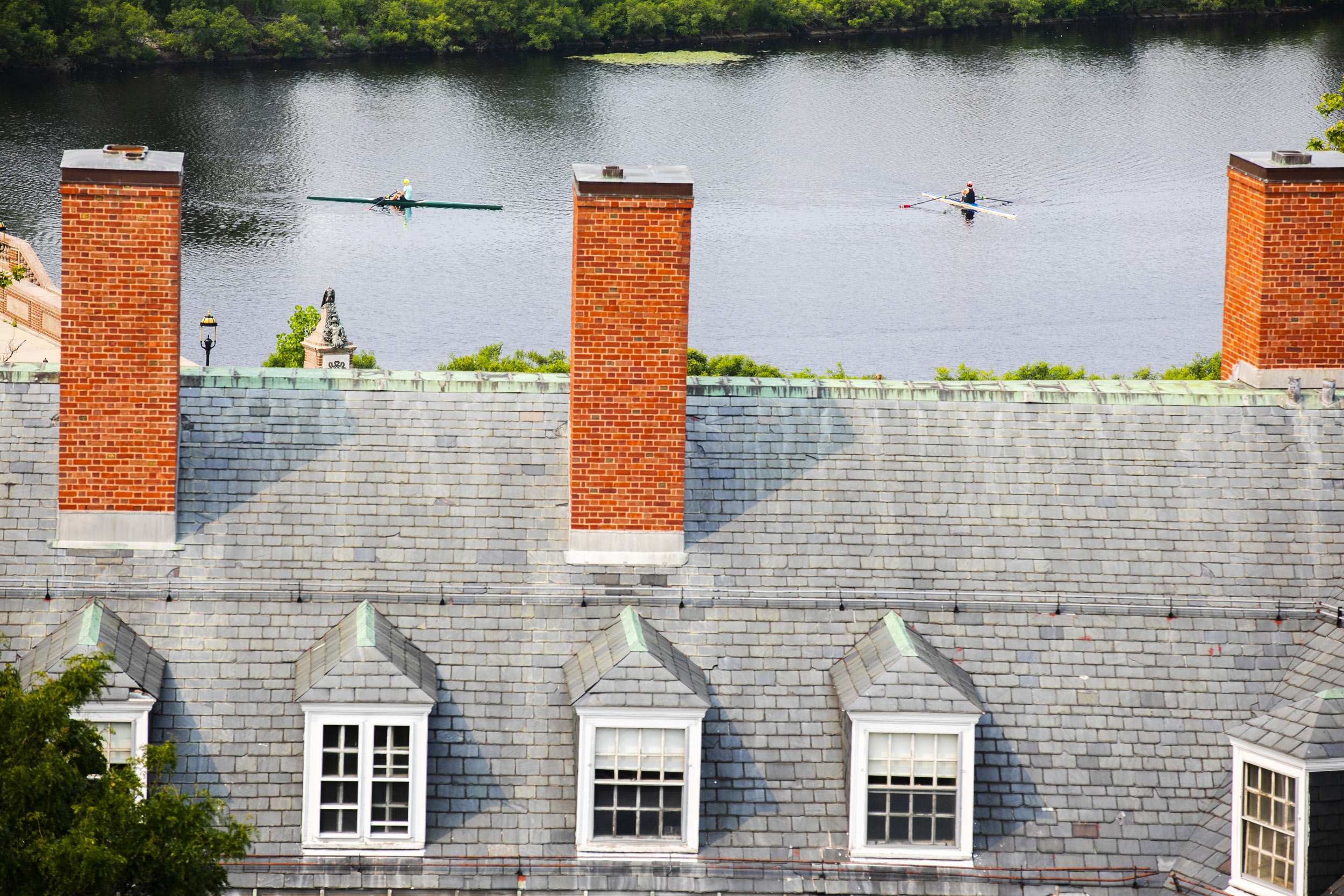 The chimneys of Eliot House frame rowers along the Charles River.