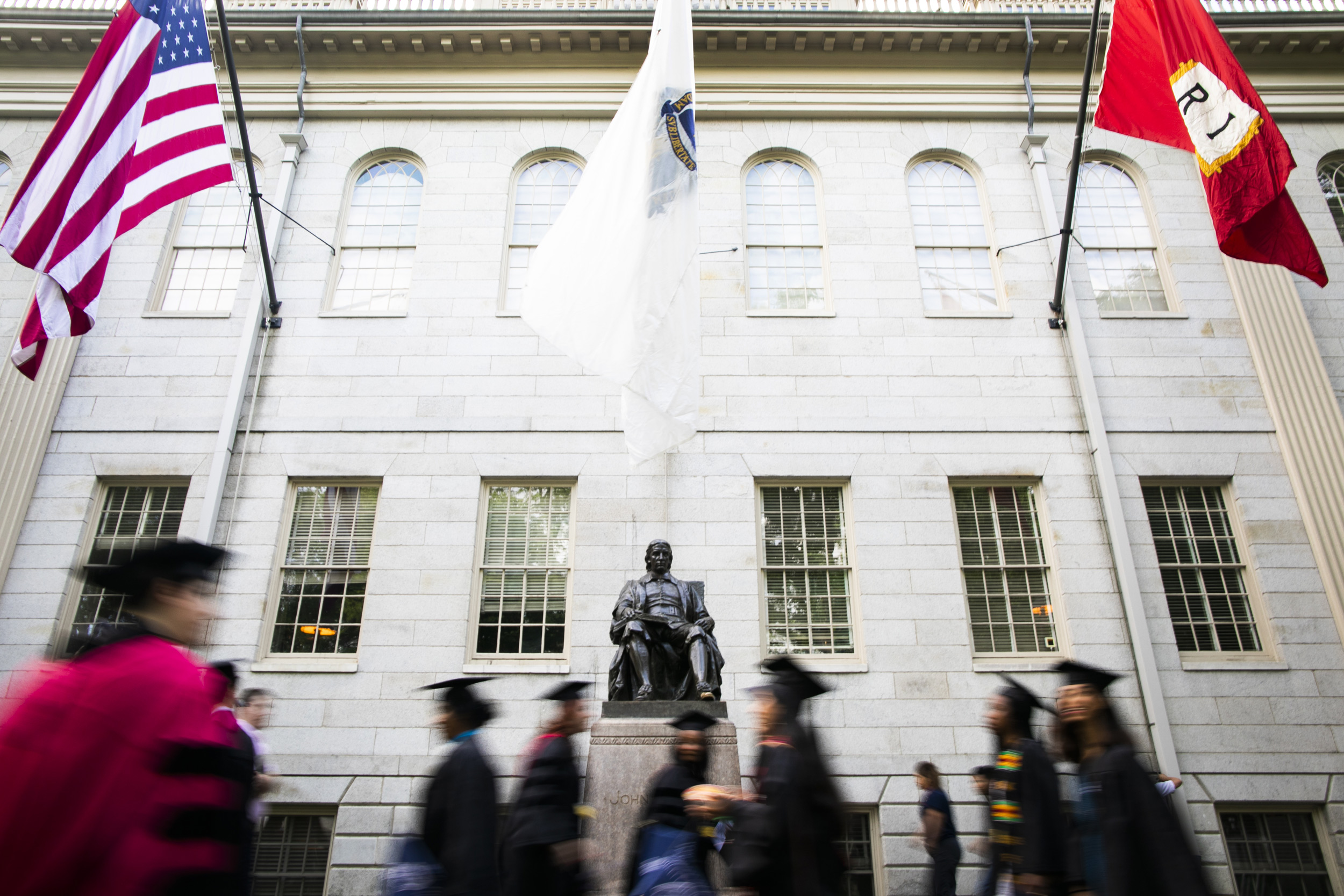 Graduates process past the John Harvard Statue.