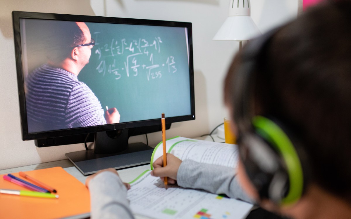 Boy looking at tutor doing math on a chalkboard via a computer.