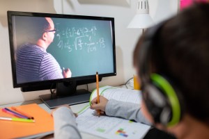 Boy looking at tutor doing math on a chalkboard via a computer.
