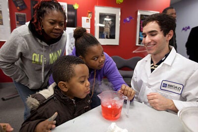 Allston resident Lude Telfort and her children, Jordan Francis, 3, and Prya Francis, 11, learn about dry ice and chemistry from Brandon Silverman '12 inside the Harvard Allston Education Portal during the Halloween-themed community event.