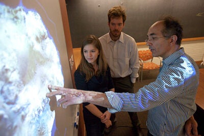 Jerry Mitrovica (right), Peter Huybers (white shirt), and graduate student Natalya Gomez (center), whose research illuminates the relationship between sea ice and climate change, look at a slide of the West Antarctic ice sheet. The researchers theorize that if the sheet melts, it will have the seemingly contradictory effect of lowering sea levels nearby, actually stabilizing the sheet.