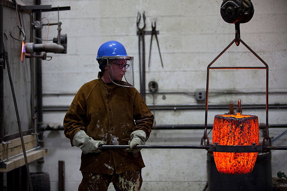 Shayla MacDonald, a member of the foundry staff, guides the glowing crucible toward the casting pit to begin the pour for the second set of works — medallions made from a lost wax casting process. 
Stephanie Mitchell/Harvard Staff Photographer
