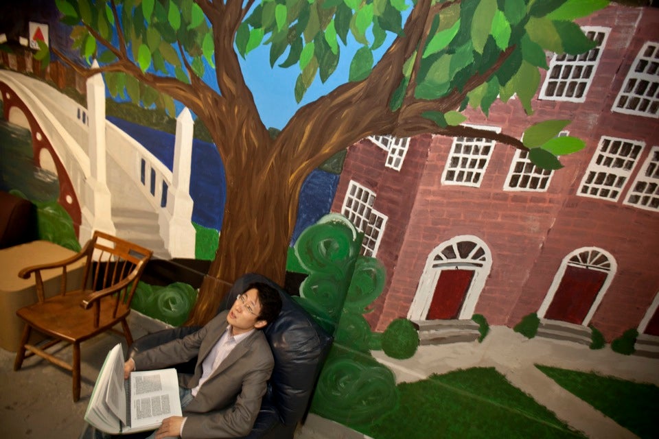 Luchen Wang `14 lounges in front of a student mural depicting Quincy House and the Weeks Bridge in the basement of Old Quincy prior to renovations.