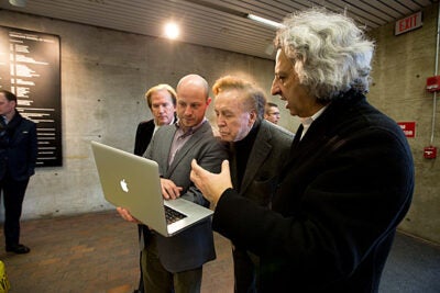 Ben Prosky (second from left), GSD's assistant dean for internal and external communications, shows John Portman Jr. and GSD Dean Mohsen Mostafavi pictures of an exhibit that is being installed in the lobby of Gund Hall. The GSD has established the John Portman Visiting Chair in Architecture in honor of Portman.