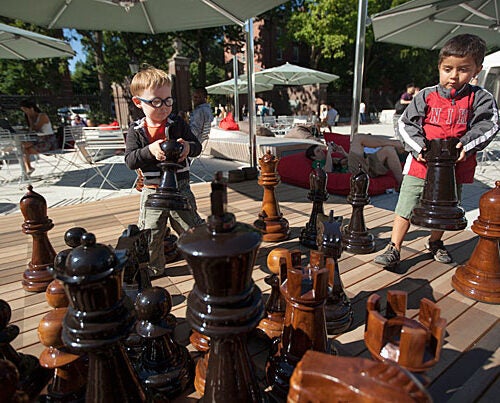 Daniel Reyes, 3 years old and Karl Ikerman, 2 (glasses) years old play a game of giant chess while harvard students use social media on their smart phones in the background at the Science Center plaza at Harvard University. Kris Snibbe/Harvard Staff Photographer