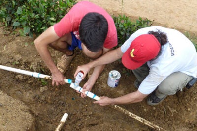 Volunteers from the Harvard chapter of Engineers Without Borders, William Jameson ’16 and Christopher Lombardo of SEAS, work to repair a water pipe leak (photo 1) at the Dominican Republic site. A drill rig is sits at the location of the new water well (photo 2). Water from three local sources was tested in January: samples from the river, small wells called tinitas, and a spring near the top of a hill. The samples showed bacterial growth (left, photo 3). Water from the newly installed well, which was tested in August 2014, was free of bacteria (right).


