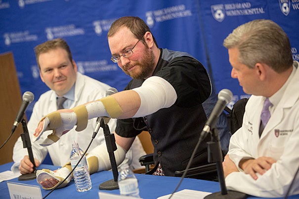 Will Lautzenheiser's moves his new left arm for reporters. Last month, Lautzenheiser received a bilateral arm transplant with the help of Simon Talbot (left), director of the Brigham’s Upper Extremity Transplant Program, and Matthew Carty (right), head of the Brigham’s Lower Extremity Transplant Program. 