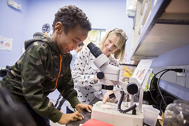 Susan Johnson (right, photo 1), manager of teaching and curriculum at the Harvard Allston Education Portal, helps  Mubeen Elamin with a microscope during a showcase of the mentoring partnership between Harvard undergraduates and Allston-Brighton residents. Mom Priscilla Anderson (from right, photo 2) watches daughter Dora Capobianco get input from Abigail Orlando '17, while Kennedy O'Neil looks on. Kawn Ang '15 (from left, photo 3) and Stella Tu '16 work with Brighton resident Mandy Lin.