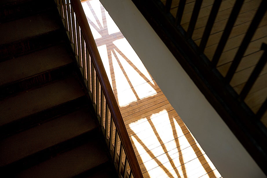Shadows from the geometric-patterned windows are elongated on the wooden floor by a stairwell.