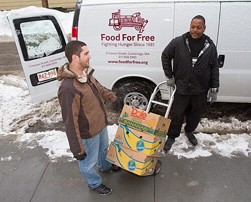 Director of programs at the Cambridge Community Center Darrin Korte (left) and Adam Collins wheel cartons of food from the Food for Free van into the center, which is one of the local organizations receiving donations from Harvard. 