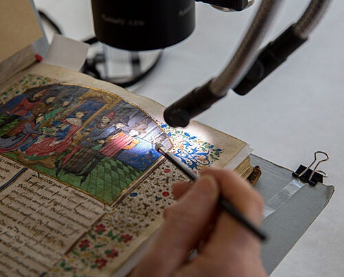 Book conservator Catherine Badot-Costello uses a microscope to work on an illuminated, bound parchment manuscript from Houghton Library. 
