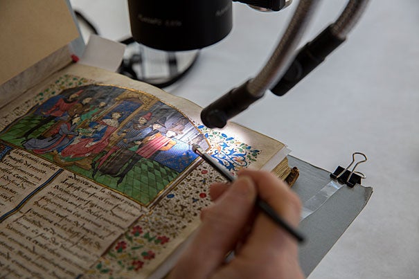 Book conservator Catherine Badot-Costello uses a microscope to work on an illuminated, bound parchment manuscript from Houghton Library. 