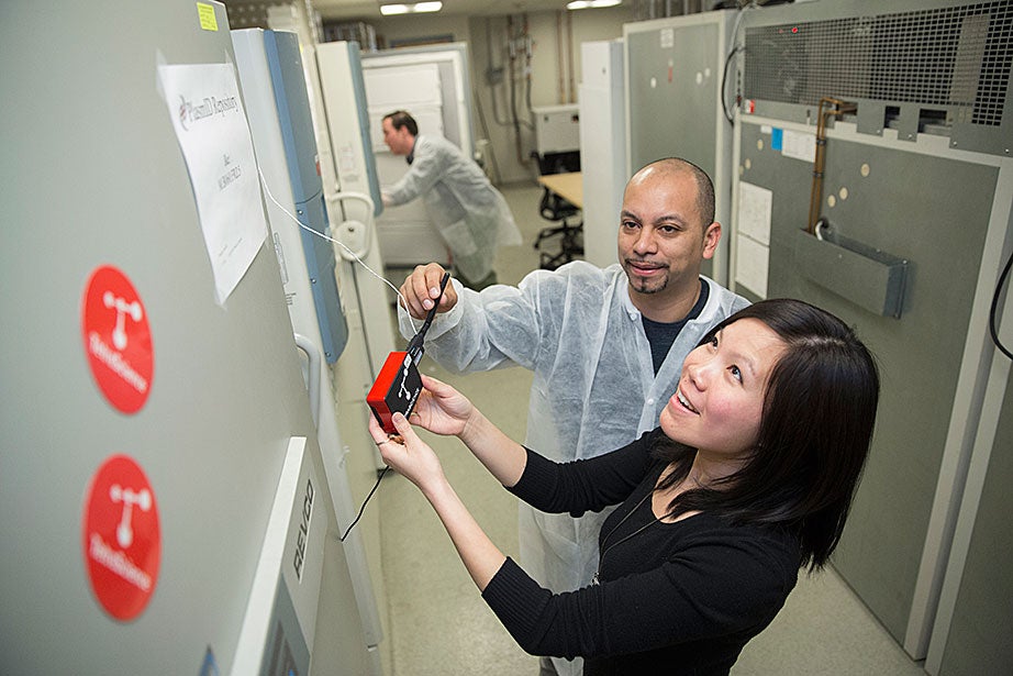 William Veguilla (left), a research assistant, and Li Qiong Chan (right), operation director of the DNA Resource Core at Harvard Medical School, work with TetraScience equipment connected to ultra-low-temperature freezers at HMS. The devices, developed by a team that included Harvard students and supported by a student sustainability grant, were developed to help researchers monitor and reduce energy using wireless technology. In the background is research assistant Alexander Reynolds. 