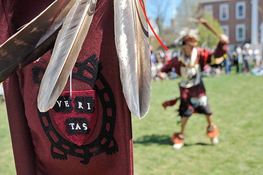 A banner bearing the Veritas turtle symbol of the Harvard University Native American Program (HUNAP) frames a dancer in Radcliffe Yard. The annual Harvard Pow Wow, now in its 21st year, honors Native American culture with traditional songs and dance. Participants include Native Americans from Harvard and members of tribes from across the United States and Canada.