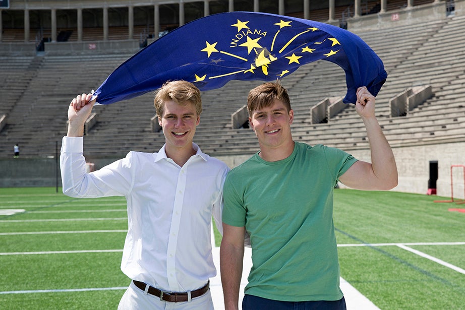 Twin sophomores Nicholas (left) and Beau Bayh '18 stand in Harvard Stadium, holding aloft the flag of Indiana, where both their father and grandfather were well-known politicians. Jon Chase/Harvard Staff Photographer