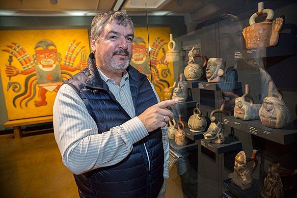 Luis Castillo, standing before ceramic pots depicting women on display at the Peabody Museum, discusses his research on high-status burials featuring female priestesses in ancient Peru and female power in the Andean culture. 