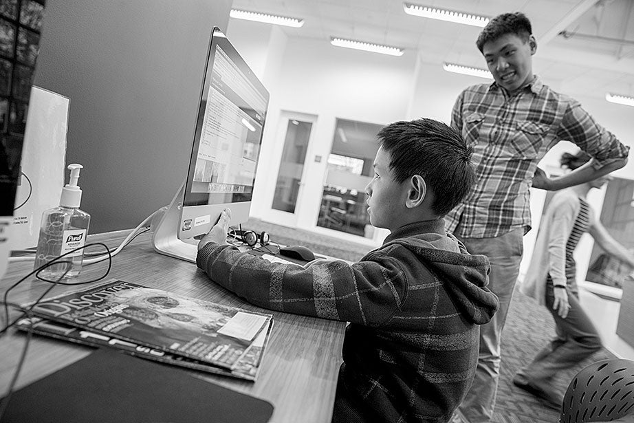 Neil plays a computer game, while Kevin looks on. Remembering his own mentor, Kevin says, “He was more than a tutor — he was a real person, he helped me to chill. He recognized my human side … he also saw my interest in biology and helped me with my studies.”