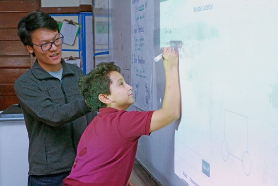 Chris Zhou ’19, an economics concentrator, helps Gardner Pilot Academy sixth-grader Jonathan Gonzalez write JavaScript functions on the classroom’s whiteboard during a Digital Literacy Project lesson. (Photo by Adam Zewe/SEAS Communications.)