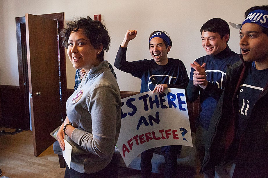 Kim Arango ’20 stands in Matthews Hall with her letter from Eliot House, while House members whoop it up in the background. Jon Chase/Harvard Staff Photographer